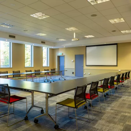A large carpeted room with U-shaped table and piano