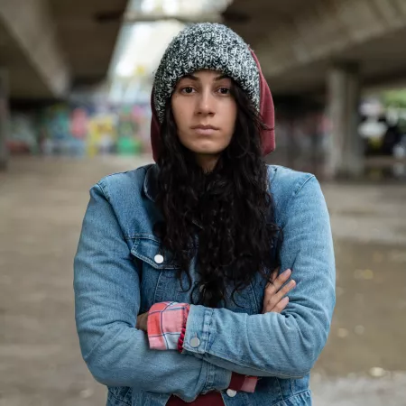 a woman with folded arms in a hoodie looks defiantly at camera