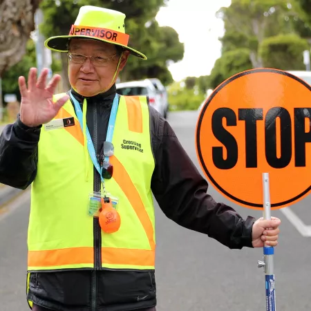 Man in fluorescent uniform with a stop sign helping children cross the road