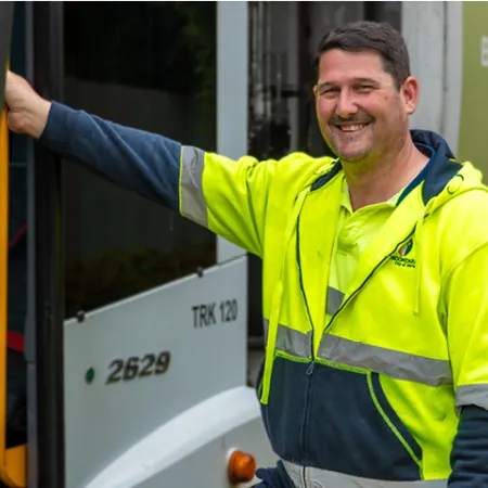 Waste truck driver in hi-vis shirt standing beside truck.