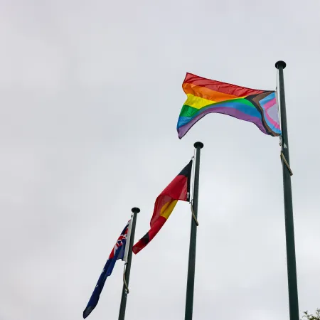 3 flags, including a rainbow flag, against a cloudy sky